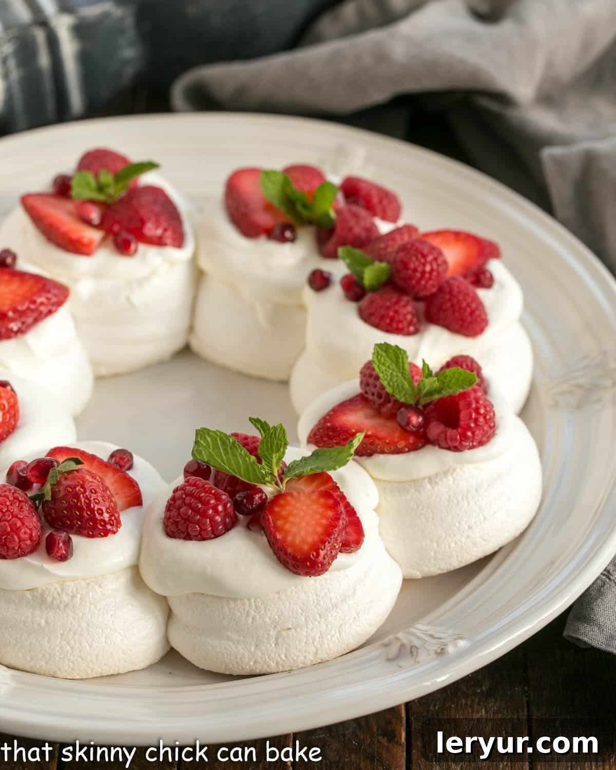 Jolly Pavlova Crown 2 Pavlova Wreath topped with berries and cream on a white serving plate, beautifully decorated for Christmas.