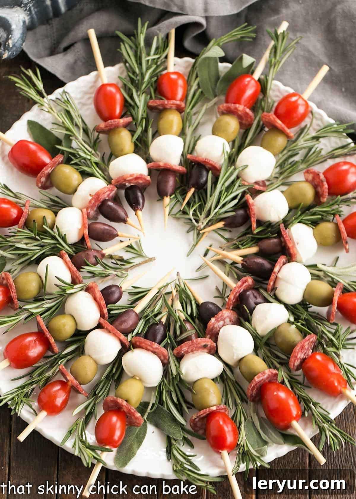 Overhead view of a beautifully arranged Antipasto Wreath with skewers radiating from the center on a white plate, adorned with rosemary.