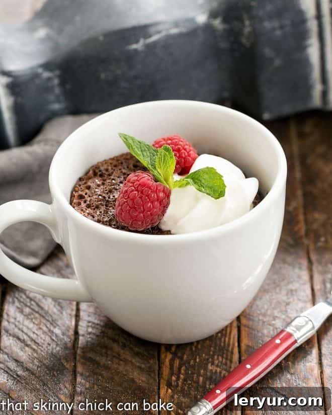Mugful of Instant Chocolate Heaven 2 Chocolate mug cake in a white ceramic cup garnished with cream, berries and mint