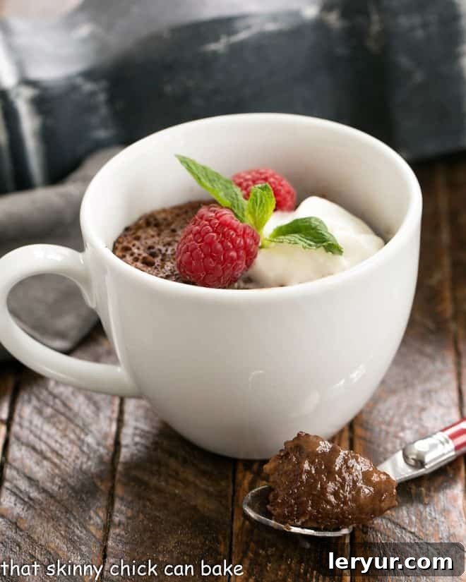 Mugful of Instant Chocolate Heaven 4 Chocolate Mug Cake garnished with cream, mint and berries with a spoonful removed