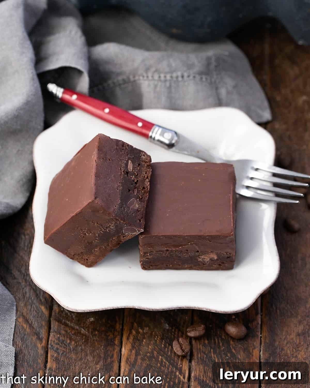 Decadent Kahlua Fudge Brownies 2 Two Kahlua fudge-topped brownies on a square white plate with a red handle fork, ready to be enjoyed.