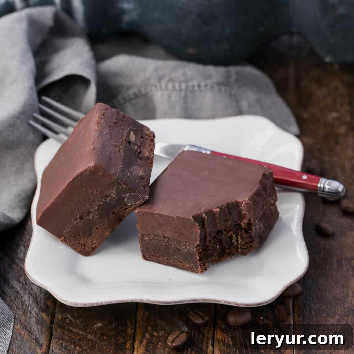 Decadent Kahlua Fudge Brownies 4 Fudge topped Kahlua brownies on a square white plate with a red handled fork, inviting a bite.