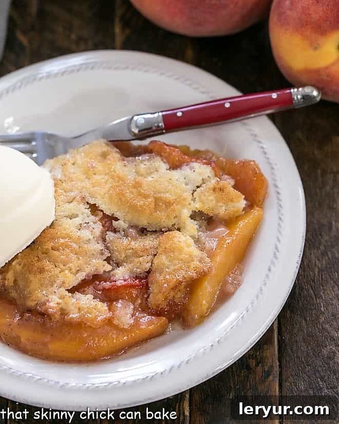 A serving of Easy Peach Cobbler on a white dessert plate, elegantly topped with a generous scoop of creamy vanilla ice cream, ready to be enjoyed.