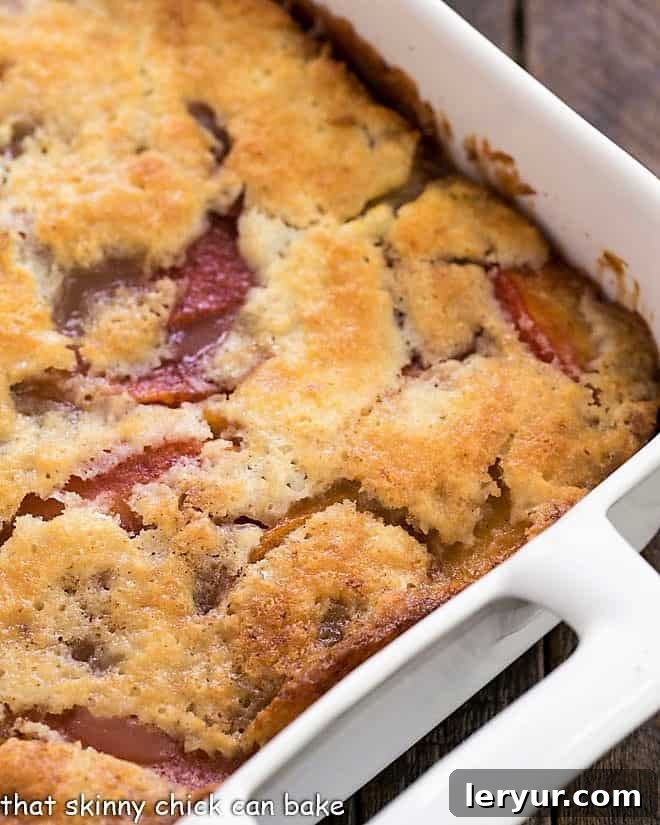 A close-up view of an easy peach cobbler baking in a white ceramic dish, showing its golden-brown, bubbly top.