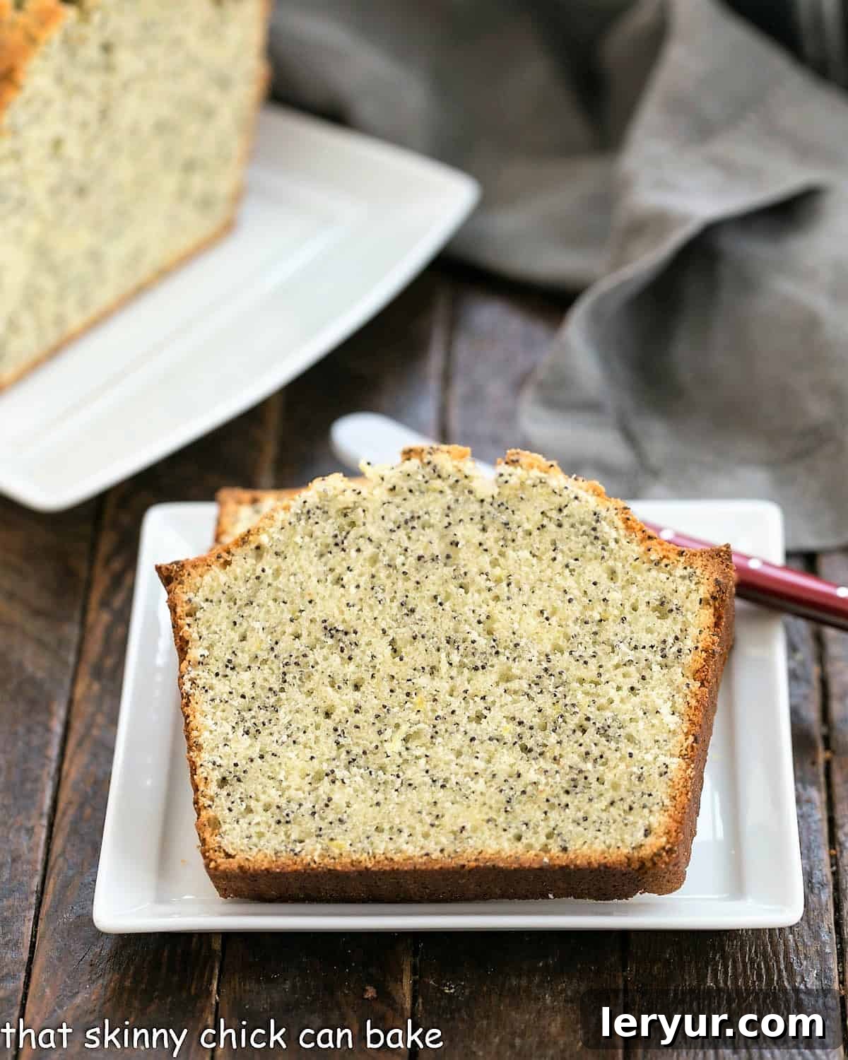 Sun-Kissed Lemon Poppy Seed Loaf 3 Two slices of poppy seed tea cake on a square white plate with a red handle knife in front of the rest of the loaf on a ceramic tray.