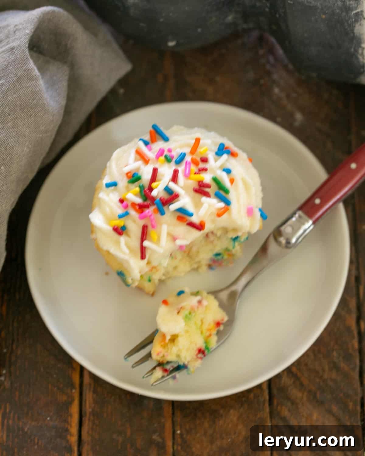 Funfetti Cupbake on a white dessert plate with a red handle fork.